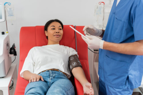 woman in blood pressure cuff sitting on medical chair near automated transfusion for IV therapy