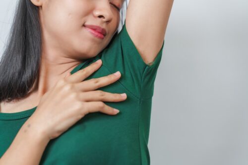 woman raising her arm and checking an underarm sweat stain caused by excessive sweating